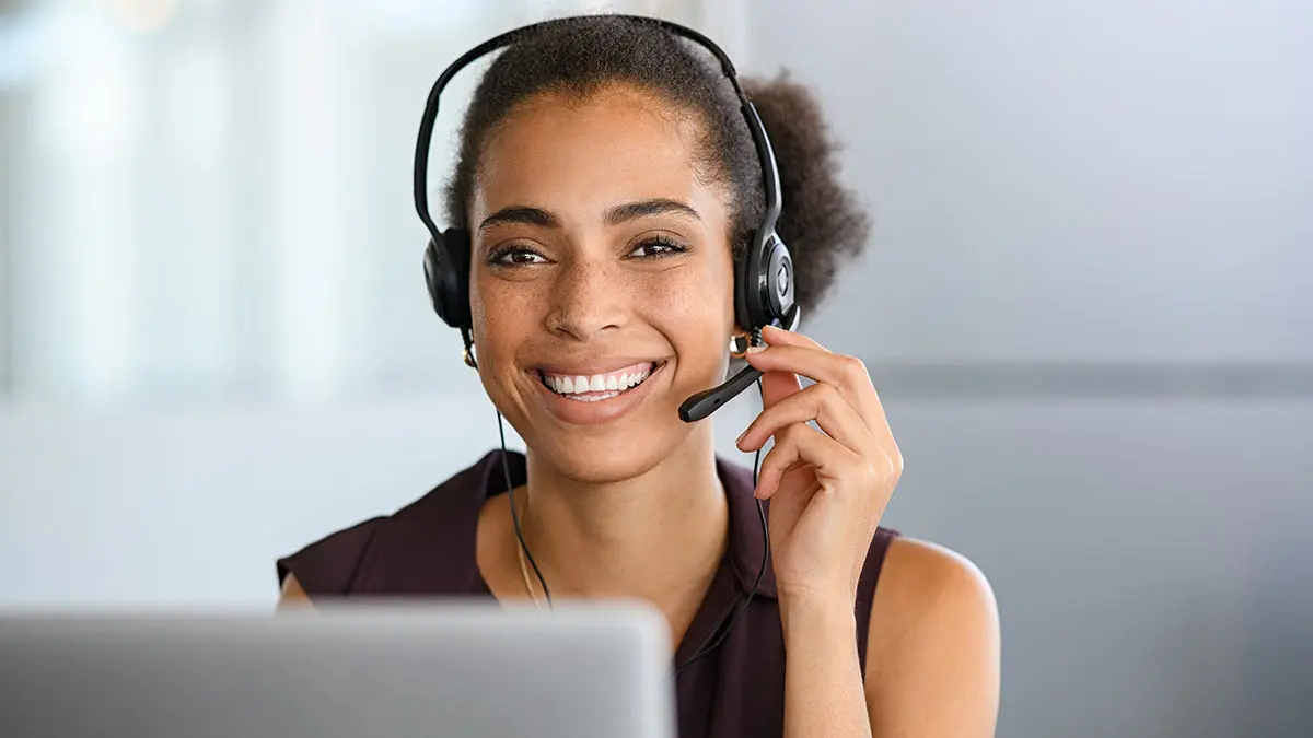 lächelnde Frau mit Headset vor Laptop