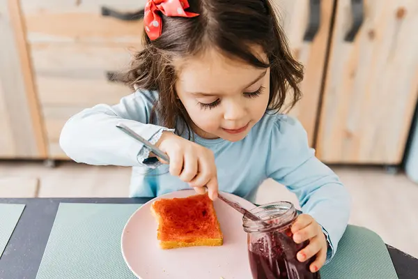 Ein Mädchen bereitet sich ein Brot mit Marmelade zu