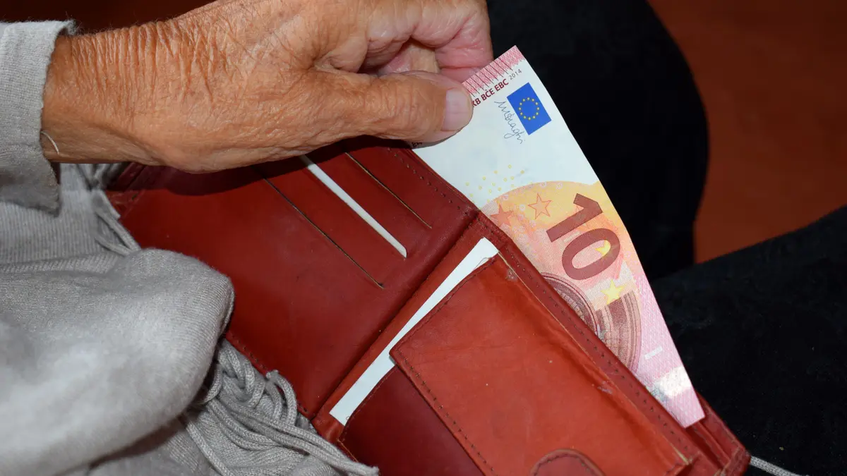 Hand einer älteren Frau zieht einen 10 Euro-Schein aus einem Geldbeutel.