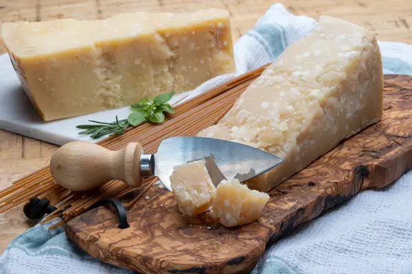 Zwei Stück Parmesan liegen auf zwei Brettern. Das vordere Stück ist mit einem Käsemesser angeschnitten.