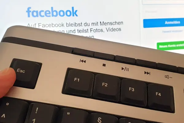 Daumen auf ESC-Taste einer Tastatur vor dem Login-Bildschirm von Facebook