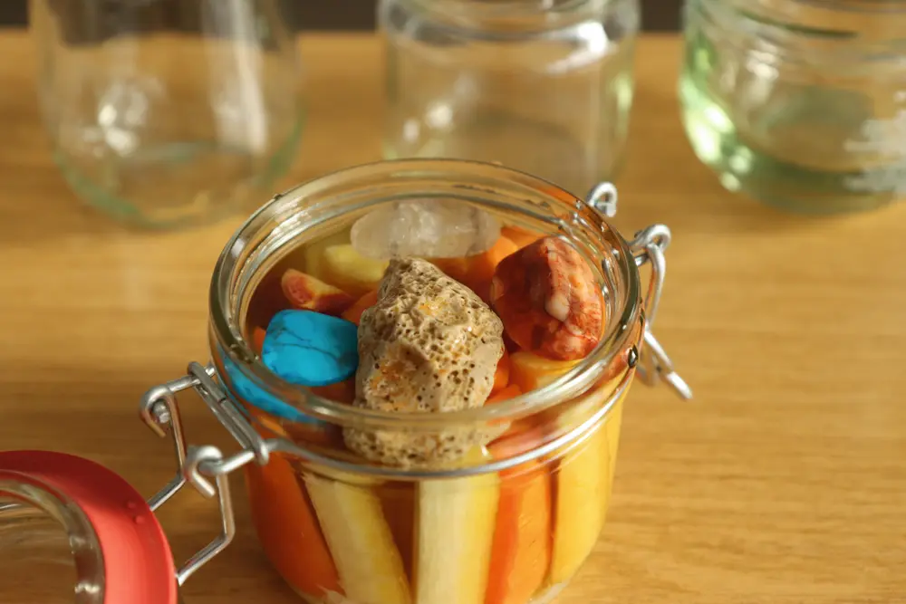 Ein offenes Einmachglas mit Gemüsesticks und Wasser. Kieselsteine halten das Gemüse unter der Wasseroberfläche.