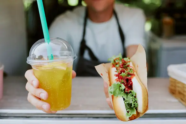 Jemand reicht einen Hotdog und einen Softdrink aus einer Imbisswagen nach draußen 