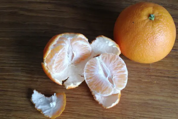 Eine zur Hälfte abgeschälte Mandarine liegt neben einer ungeschälten Mandarine auf einem Holztisch