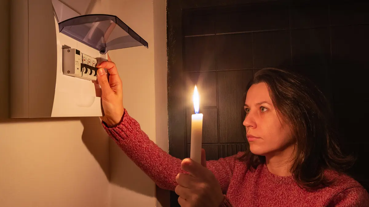 Eine Frau steht mit Kerze in der Hand vor einem Sicherungskasten.