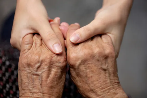 junge Hände halten fürsorglich die Hände einer alten Person