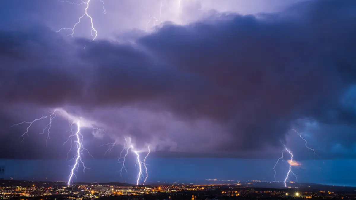 Auf dem Foto sind mehre Blitze zu sehen, am unteren Bildrand Häuser. Der Himmel ist dunkel.