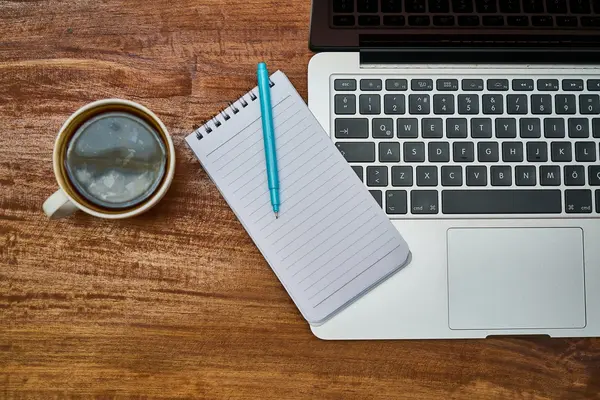 Laptop, Block und Kaffeetasse auf einem Schreibtisch
