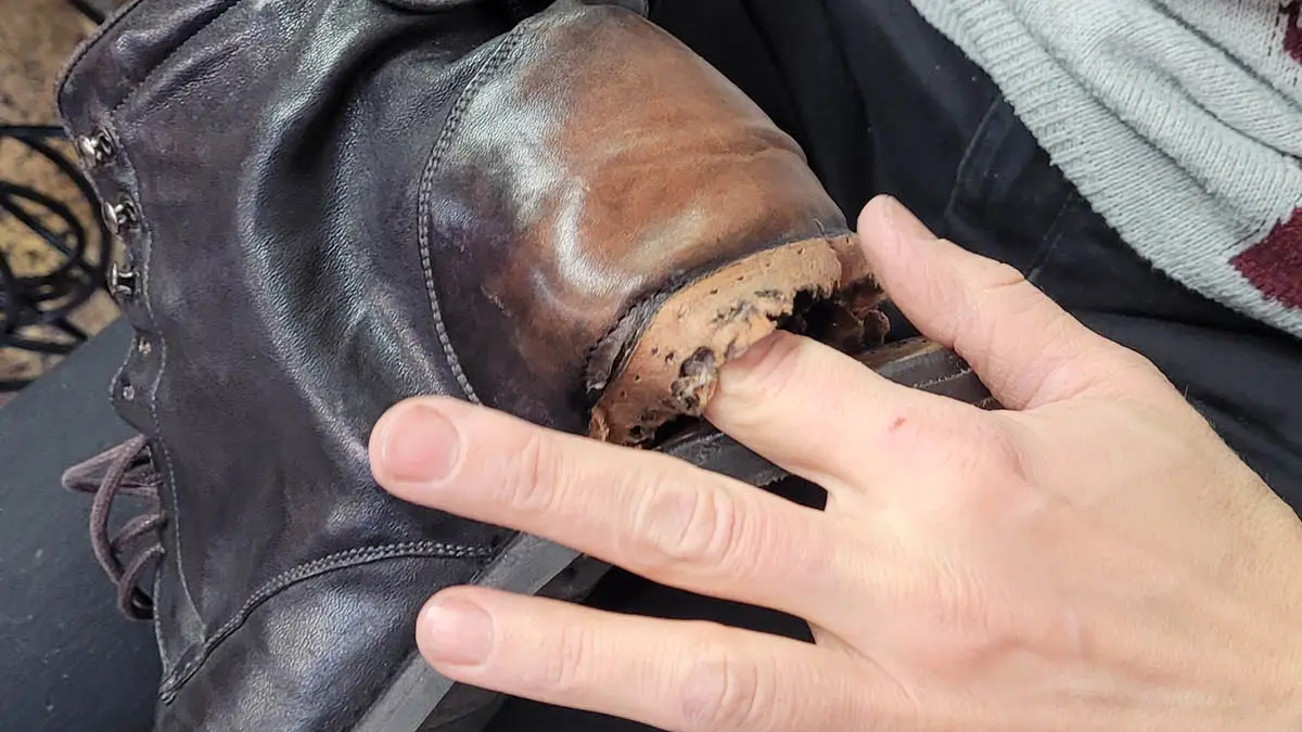 Jemand steckt den Finger in ein Loch in einem Schuh