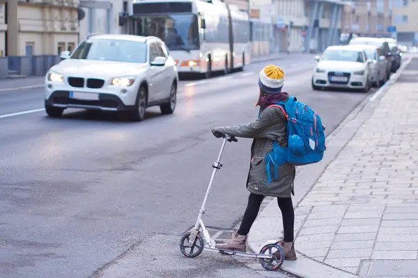 Kind überquert auf dem Schulweg mit einem Roller die Straße