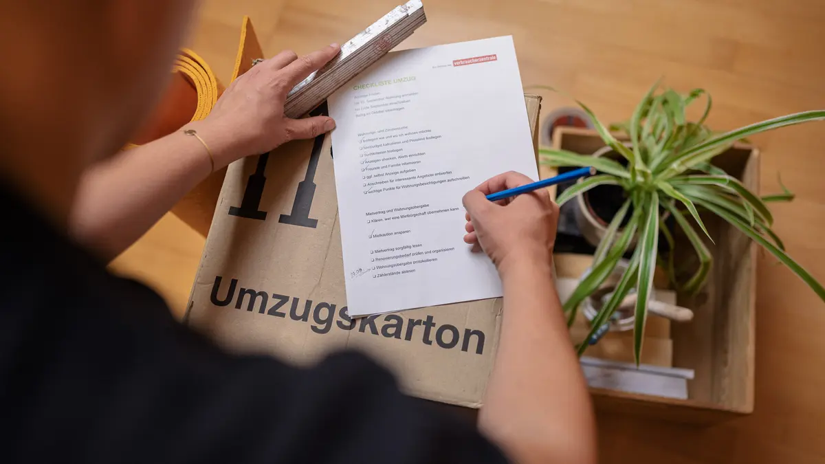 Mann hakt Umzugs-Checkliste auf Umzugskarton ab