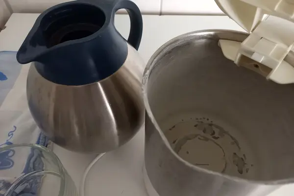Neben einer Teekanne steht ein geöffneter Wasserkocher. In ihm sieht man deutliche Kalkspuren.