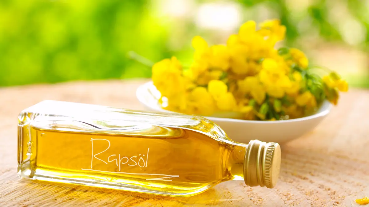 Eine Flasche Rapsöl liegt vor einer Schale mit Rapsblüten.