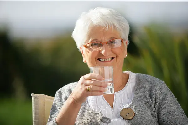 Seniorin hält Glas Wasser in der Hand und lächelt