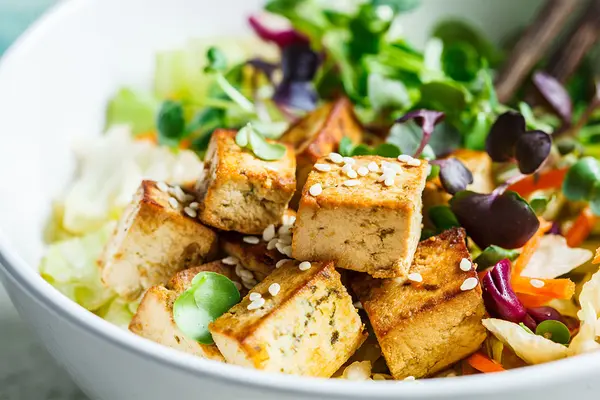 Schüssel mit Tofu-Salat. Im Hintergrund ragen Essstäbchen aus der Schüssel