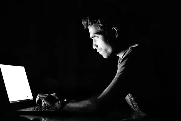 Düstere Schwarz-Weiß-Aufnahme eines Mannes, der vor einem Laptop sitzt