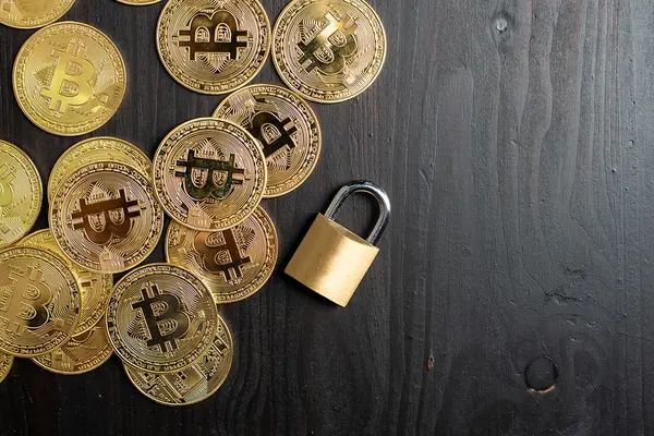 Bitcoin-Münzen und ein Vorhängeschloss auf schwarzer Tischplatte