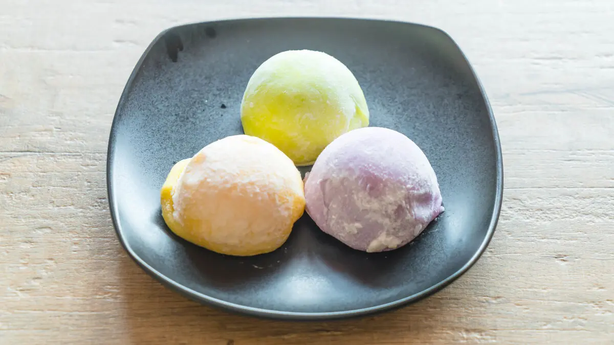 Drei Kugeln Mochi-Eis auf einem dunklen Teller.