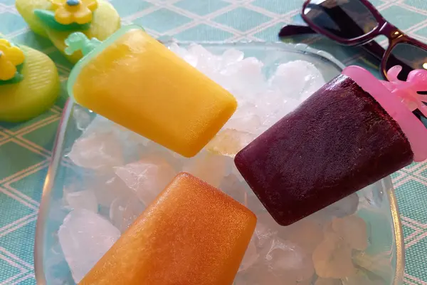 Auf einer Schüssel mit Eiswürfeln liegen drei bunte, selbstgemachte Popsicles.