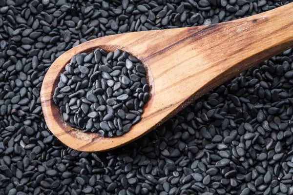 Um und auf einem Holzlöffel liegen schwarze Sesamkörner.