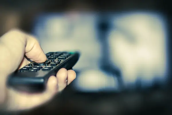 Jemand schaltet den Fernseher über die Fernbedienung an.