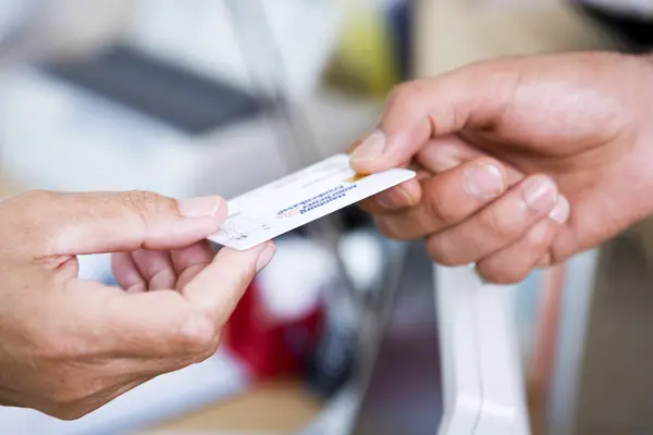 Hand überreicht die Versichertenkarte der Krankenkasse beim Arzt