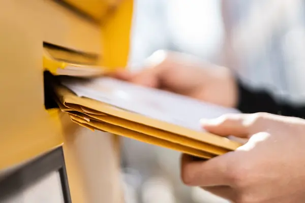 Hände, die Briefe in einen Briefkasten werfen