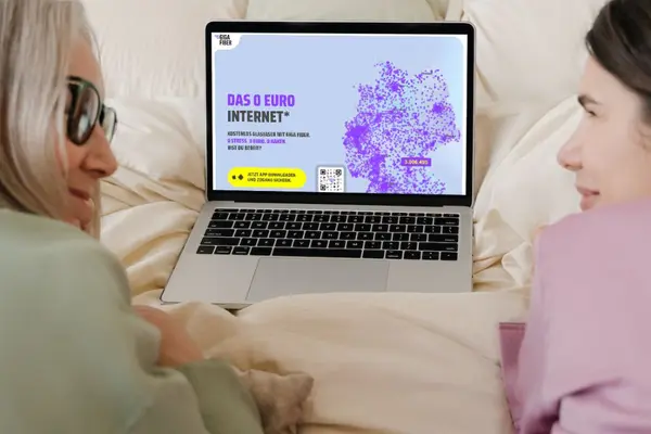 Zwei Frauen liegen vor einem Laptop, der die Internetseite der Firma Giga Fiber zeigt.
