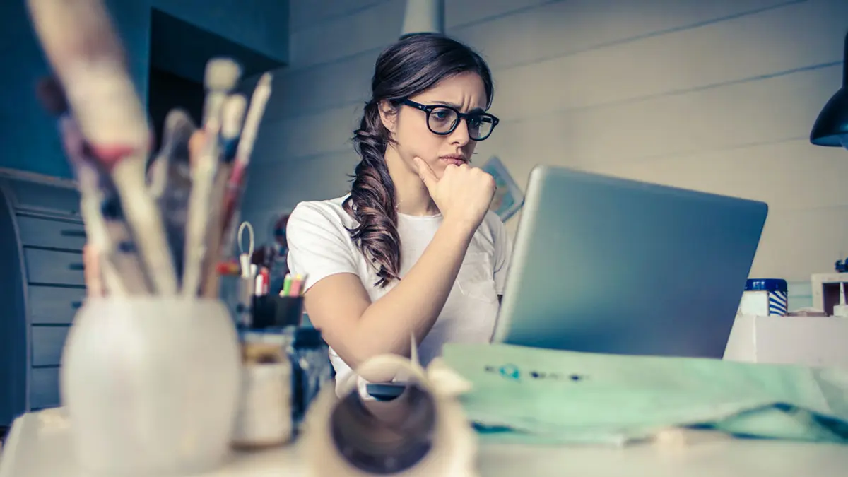 Eine Frau sitzt mit kritischem Blick am Schreibtisch vor ihrem Laptop