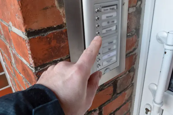 Hand, die eine Klingel an einem Mehrfamilienhaus drückt