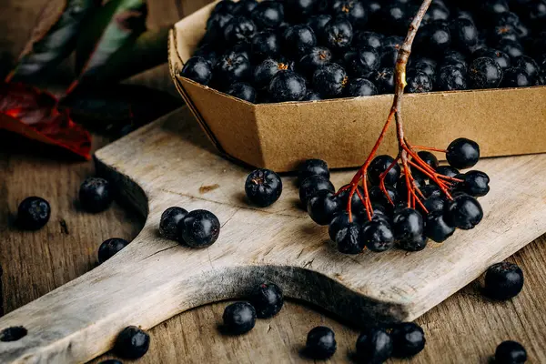 Eine Schale mit Aroniabeeren steht auf einem Holzbrett.