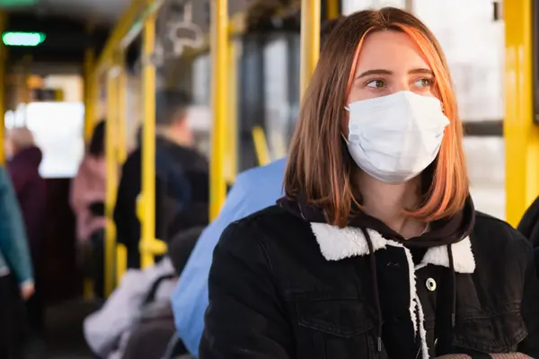 Eine Frau sitzt in einem Bus und  trägt eine Schutzmaske.