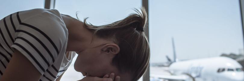 eine Frau mit den Kopf auf den Knie (traurig) im Hintergrund ein Flugzeug