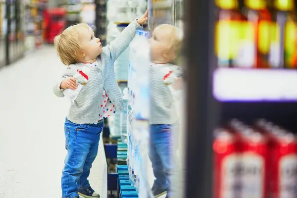Ein Kind steht in einem Supermarkt und greift nach oben ins Regal 