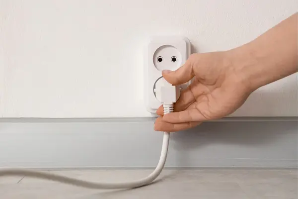 Frauenhand zeiht Stecker aus Steckdose an heller Wand
