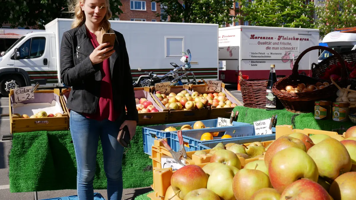 Junge Frau mit Smartphone auf dem Wochenmarkt