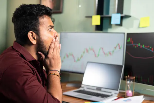 Mensch sitzt vor Computerbildschirmen mit Trading-Kurven und ist schockiert