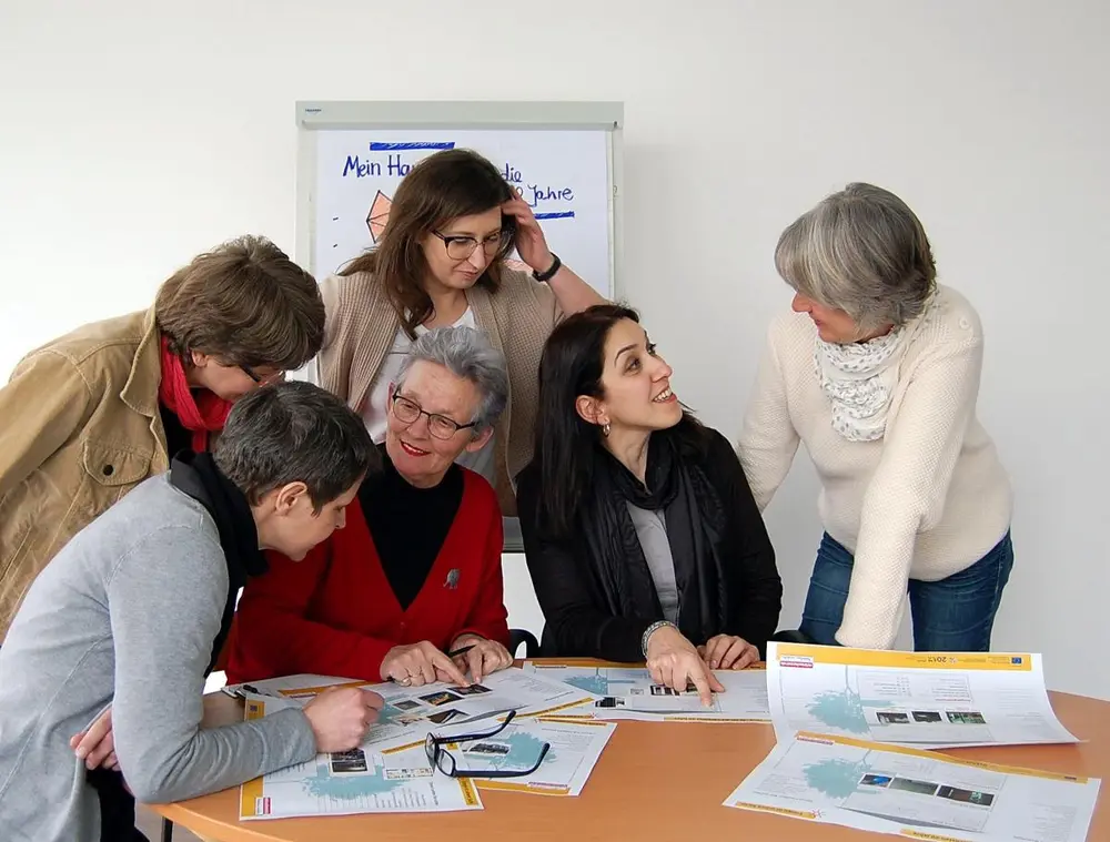 sechs Frauen sind um Tisch gruppiert und sehen sich Baupläne an