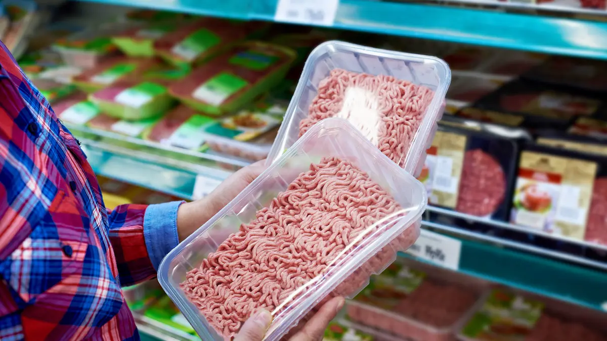 Jemand kauft im Supermarkt ein und hält zwei Packungen Hackfleisch in der Hand.
