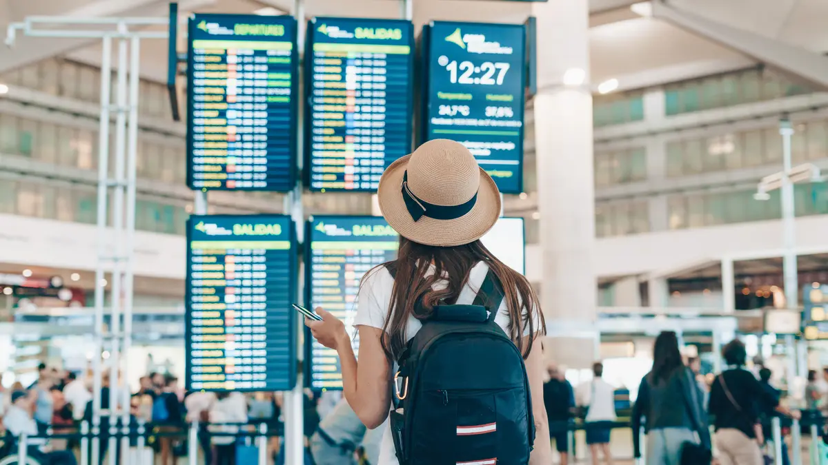 Frau steht am Flughafen und schaut auf Anzeigetafel