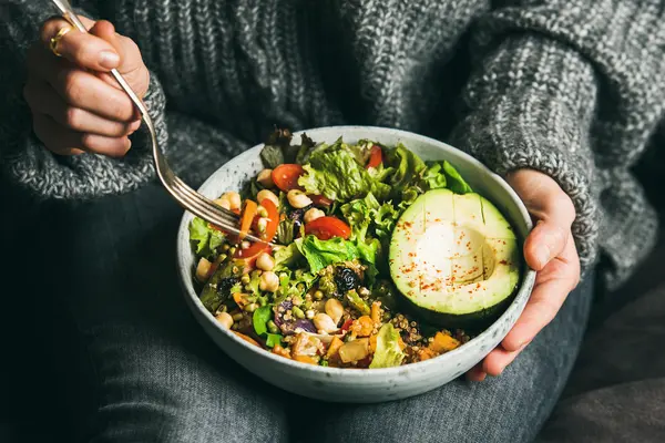 Frau hält eine Schüssel mit einem veganen Gericht in einer Hand und in der anderen eine Gabel