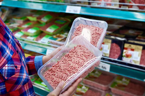 Jemand kauft im Supermarkt ein und hält zwei Packungen Hackfleisch in der Hand.