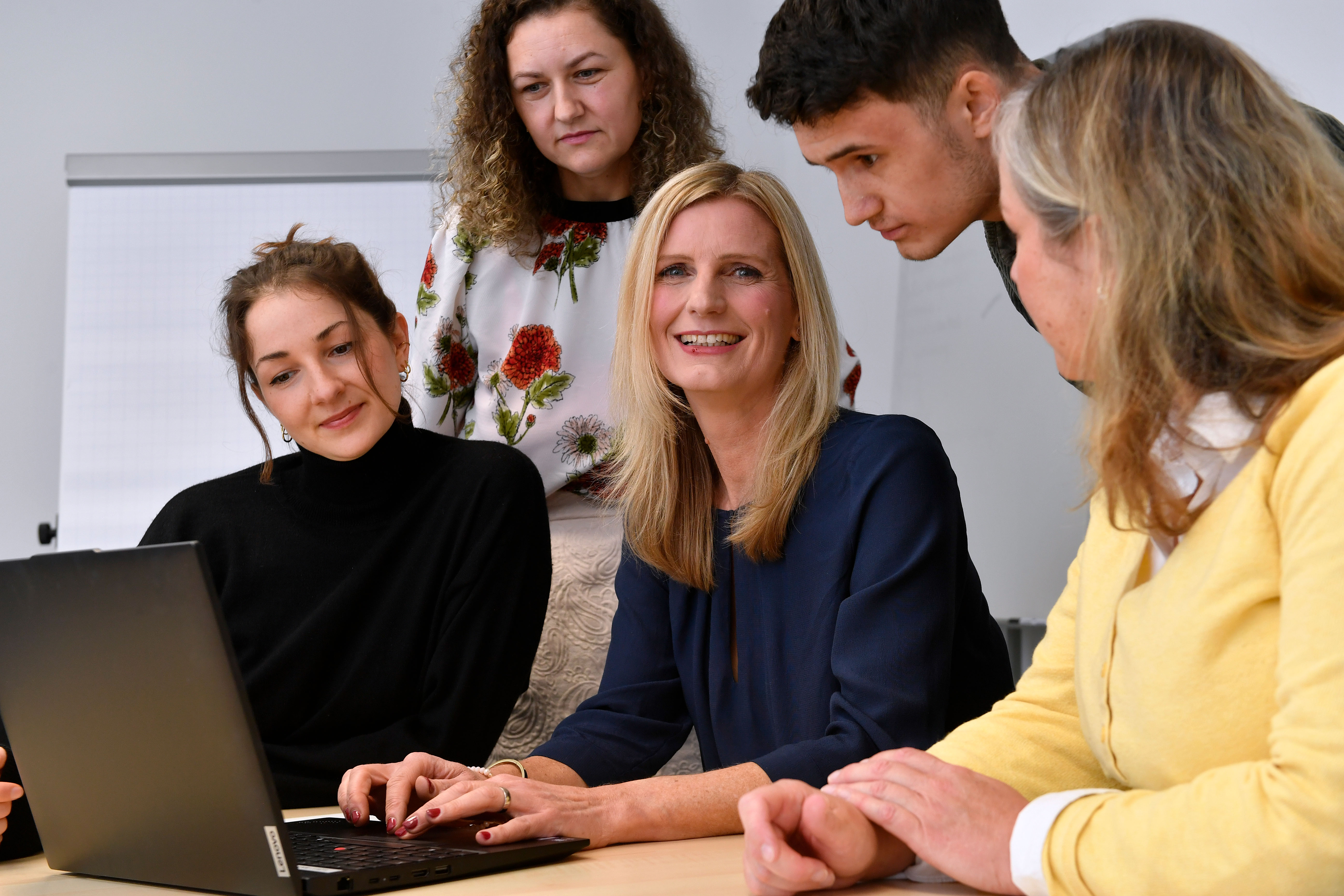 Fünf Mitarbeitende der Verbraucherzentrale Bayern arbeiten am Laptop. Die Frau in der Mitte lächelt in die Kamera
