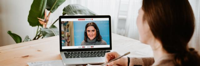 Frau sitzt mit Laptop an einem Tisch und unterhält sich per Video-Chat.