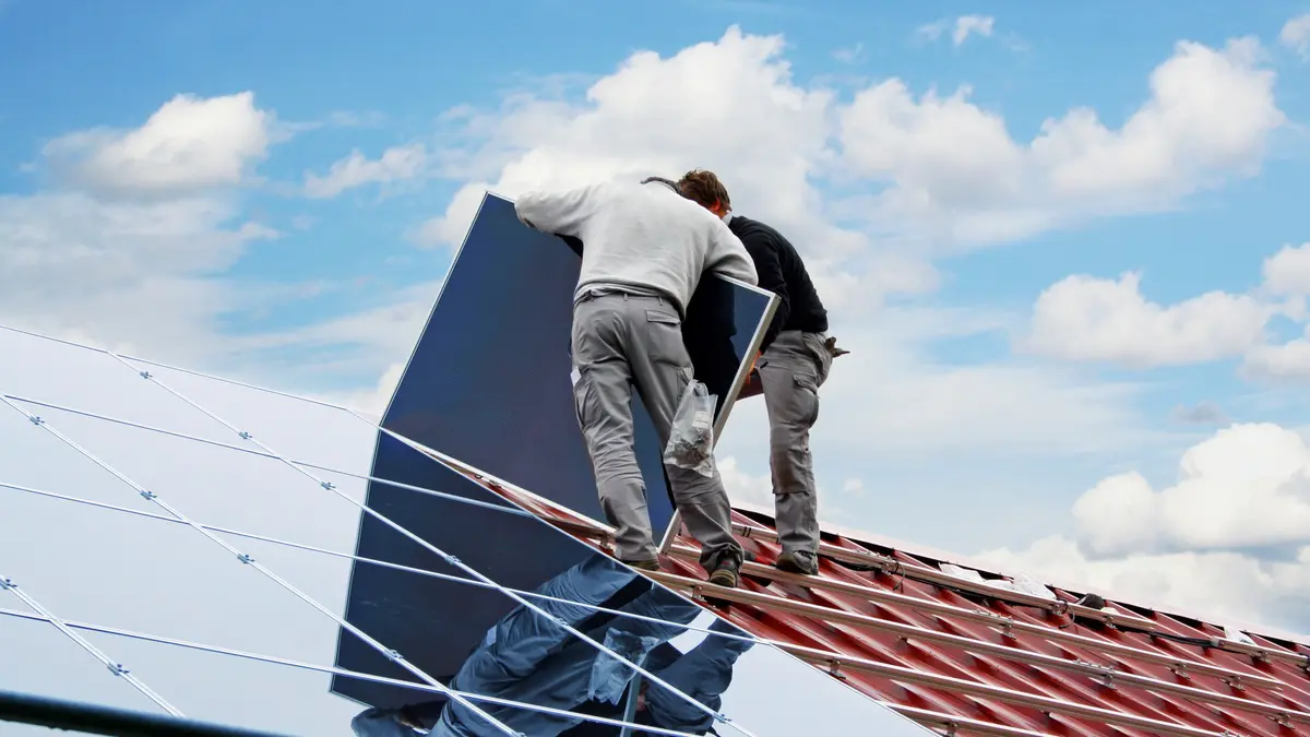 Zwei Handwerker montieren eine Solaranlage auf einem Hausdach