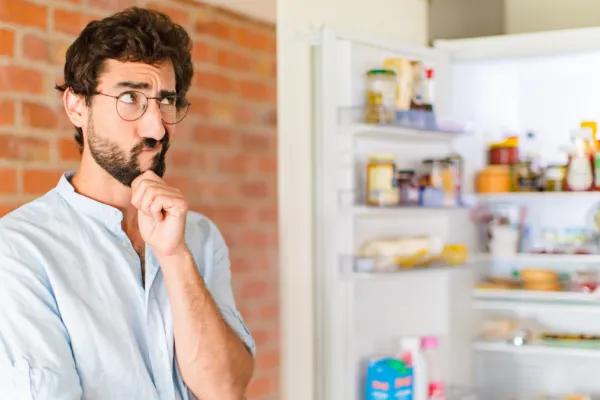 Ein Mann steht nachdenklich vor einem geöffneten Kühlschrank