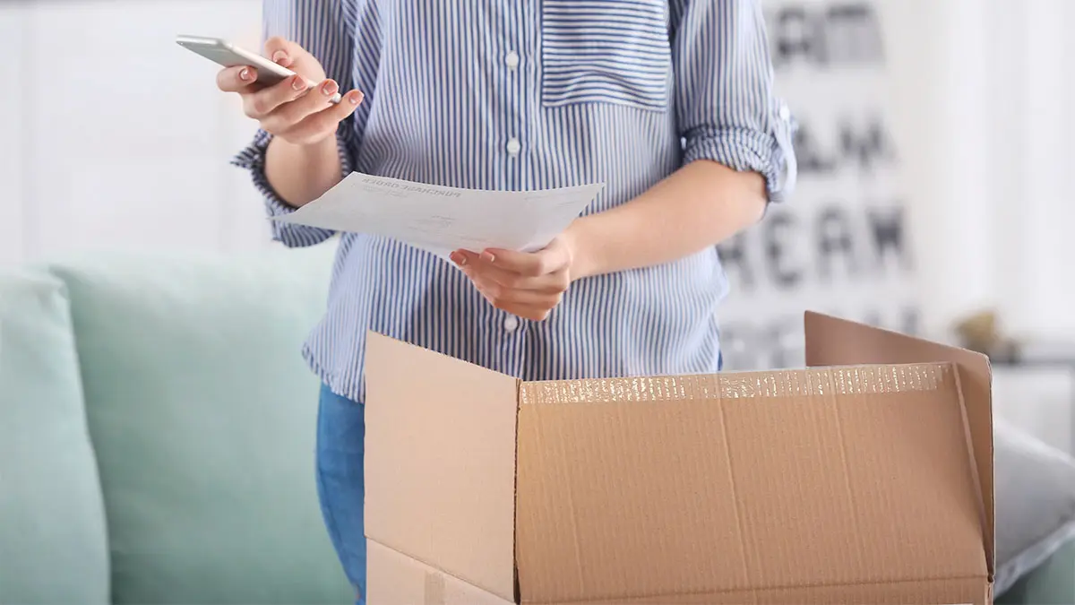 Frau hält Smartphone und öffnet ein Paket