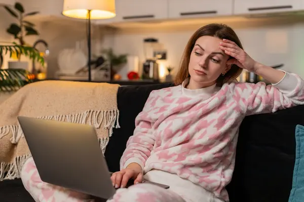 Frau sitzt auf dem Sofa und schaut kritisch auf einen Laptopbildschirm