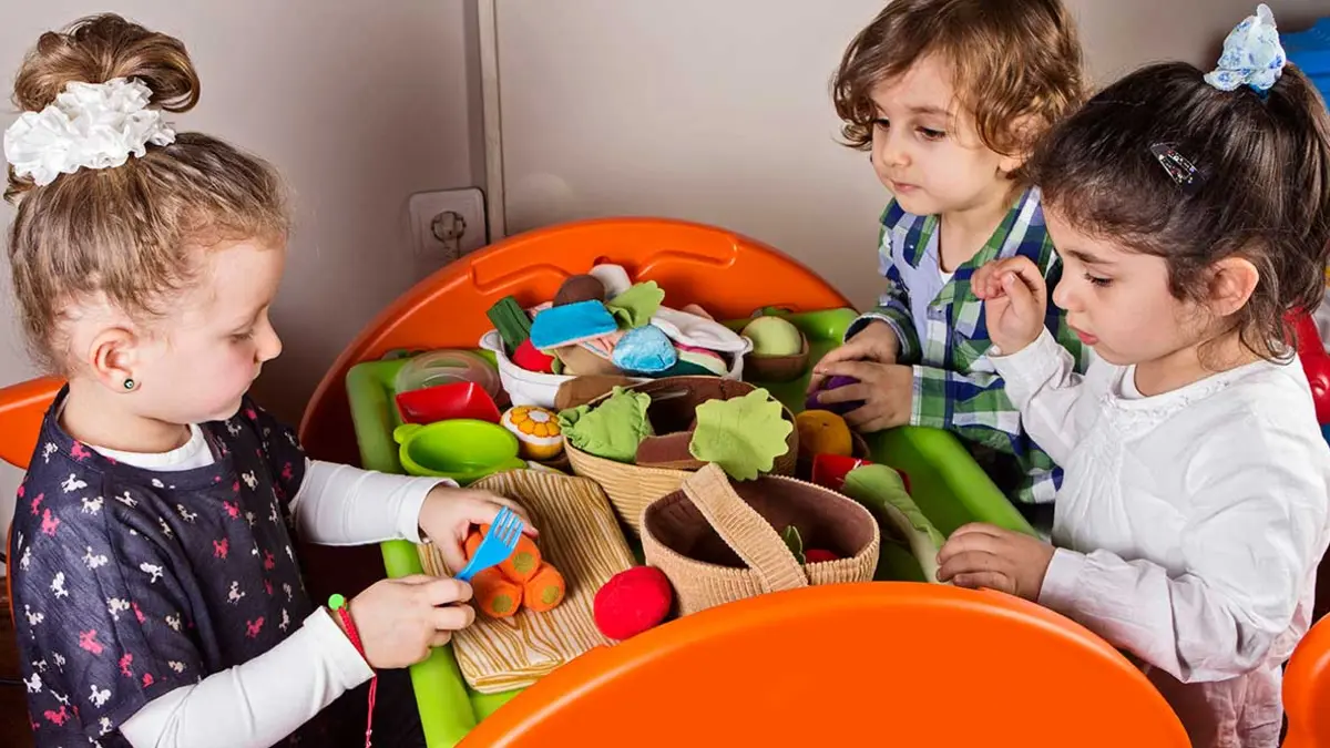 Kita-Kinder sitzen an einem Tisch und bereiten mit Spielzeug-Gemüse essen zu