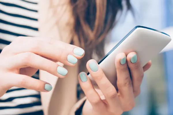 Frau mit lackierten Fingernägeln hält Handy in der Hand